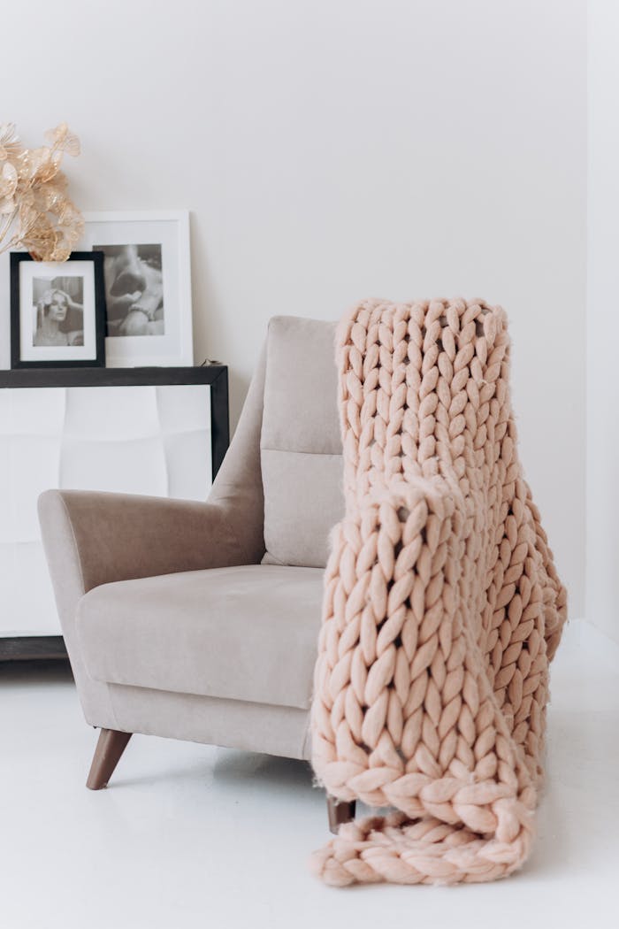 A modern beige armchair draped with a knitted throw blanket in a cozy interior setting.